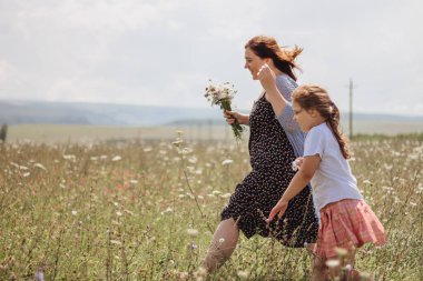 Genç bir kadın ve tarladaki bir kız çiçek topluyor.