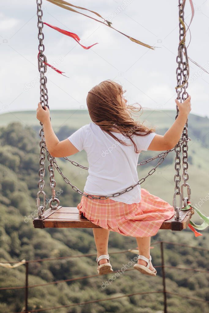 Girl rides on a swing over a cliff in the mountains