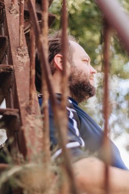 Sakallı adam merdivenlerin arkasında buhar yapıyor.