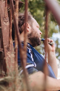 Sakallı adam merdivenlerin arkasında buhar yapıyor.