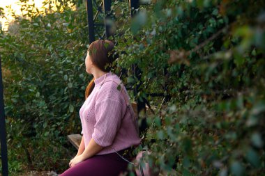 Yeşil yapraklı bir ağacın altında oturan bir kız.