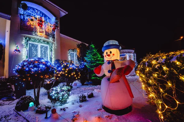 House Adorned with Christmas Holiday Lights and Decorations including Santa Snowman and Giant Trees Illuminated at Night.Christmas house