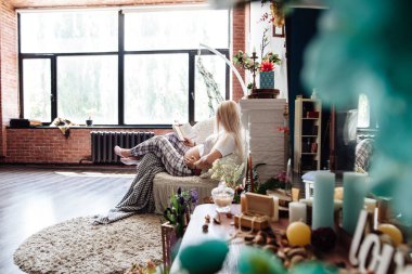 Oturma odasında kitap okuyan hamile bir kadın kanepede yatıyor. Genç, hamile bir anne hamilelik ve doğum üzerine bir kitap okuyor. Hamilelik kavramı, annelik, dinlenme, beklenti.