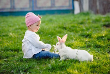 Güneşli bir günde yeşil çimenlerin üzerinde tatlı küçük bir kız. Parktaki tavşanların arka planında mutlu bir bebek. Dışarıdaki bir yaşındaki bir bebeğin portresi..