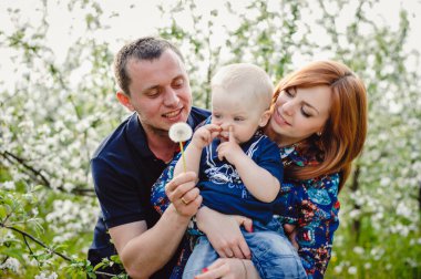 Mutlu ebeveynler ve bebek dışarıda birlikte rahatlıyor. Mutlu genç bir aile bahar bahçesinde piknik yapıyor, parkta. Anne, baba ve oğul portresi. Aile tatili.