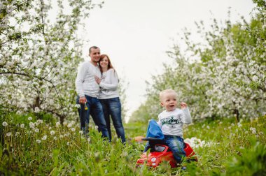 Baba, anne ve küçük oğlu dışarıda birlikte eğleniyorlar. Baharda çiçek açan bahçede aile yürüyüşü, park. Dışarıda mutlu bir aile. Aile, tatil kavramı