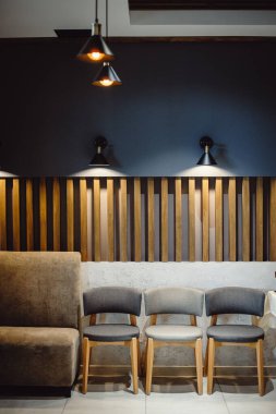 Sakin pastel renkler ve basit çizgilerle modern iç mekan. Duvarın karşısında duran üç gri sandalye retro lambalarla aydınlatılıyor. Oturma odası iç dizayn kompozisyonu. Modern ev dekorasyonu