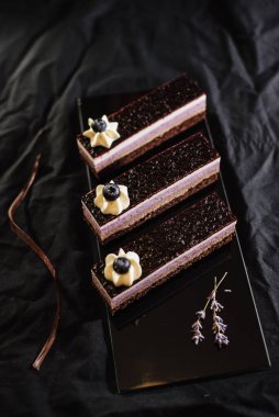 Siyah arka planda üç çikolatalı kek. Yabanmersinli kremalı kek. La carte tatlılarında opera pastası, siyah arka planda pastalar. Seçici odak