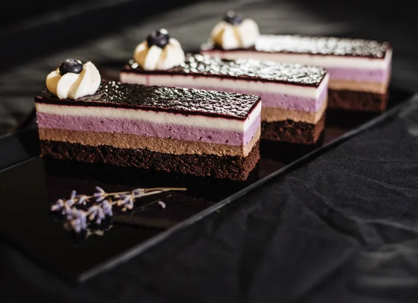 Three chocolate cakes on a black background. Mousse cake with blueberries. Opera cake at the a La carte desserts , cakes on a black background.