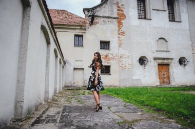 Elbiseli güzel esmer, eski kalenin avlusuna gider. Gri vintage binanın arka planında siyah elbiseli şık bir kız. Büyük üzgün gözler..