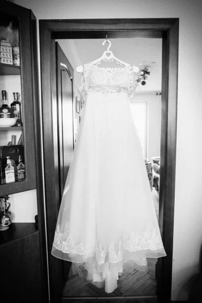 花嫁だ 部屋のハンガーにかかって美しい古典的なレースシルクのウェディングドレス 朝の準備結婚式のコンセプト 白黒写真 フィルムノイズ — ストック写真
