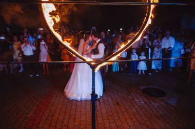 Yanan bir kalbin arka planında yeni evlenmiş sevgililerin siluetinin düğün portresi. Damat gelini ateşin yanında kucaklıyor. Ateşli aşk, havai fişek gösterisi. Gelin ve damat bir ateş gösterisinde