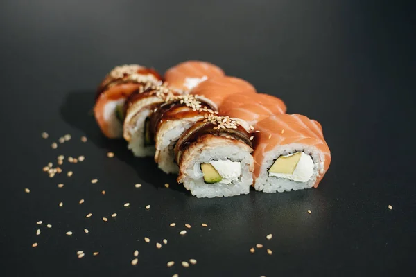 Traditional sushi - Philadelphia with salmon, avocado and cheese. Japanese cuisine. Rainbow Sushi Roll with salmon, eel, tuna, avocado, Philadelphia cream cheese on a black background. Sushi menu.