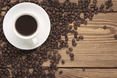 Tahta desenli masanın üzerinde kahve çekirdekleri olan bir fincan kahve. Üst Manzara. Boşluğu kopyala.