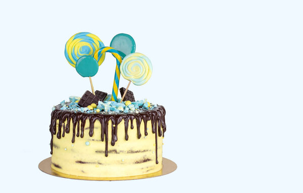 Birthday cake with yellow and blue decor and chocolate icing on a white isolated background. Cake decorated with lollipops copy space.
