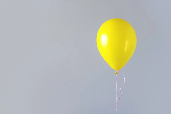 A yellow balloon against a gray wall copy space.