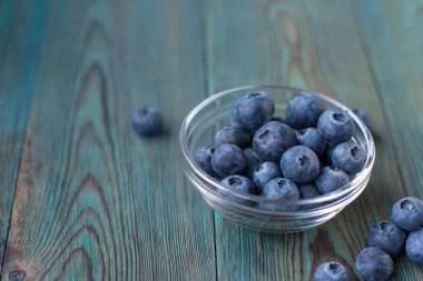 Küçük cam bir kase olgun yaban mersini mavi ahşap masa üzerinde fotokopi alanı.