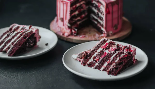 Čokoládový dort s růžovou smetanou a glazurou posypaný cukrovinkami. Kousek dortu na talíři. — Stock fotografie