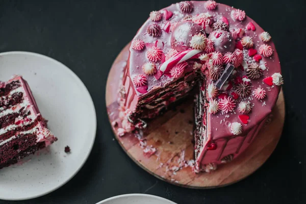 Čokoládový dort s růžovou smetanou a glazurou posypaný cukrovinkami. Kousek dortu na talíři. — Stock fotografie
