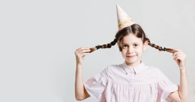 Doğum günü şapkalı esmer, modaya uygun bir kız. Gülümsüyor ve oynaşıyorlar. Beyaz bir stüdyo geçmişinde. Bir yazıt için yer.