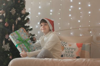 Komik, koyu saçlı bir kız hediyelerle yatakta oturuyor, Noel ağacının yanında. Yastığın üzerine yeni yılınız kutlu olsun! Bir yazıt için yer.