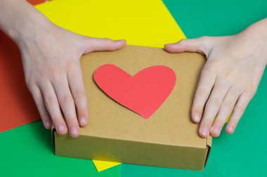 Çocuk kırmızı kalpleri makasla kesiyor ve bir hediye veriyor. Yakın plan. Renkli arka plan. Bir yazıt için yer.