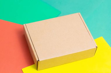 Hediye olarak küçük boş bir karton kutu. Çok renkli bir arka planda. Yakın plan. Bir yazıt için yer.
