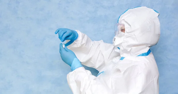 身穿蓝色背景的白色防护服的医务工作者 戴上呼吸器和手套 准备注射器 准备一套疫苗 登记的地方 — 图库照片