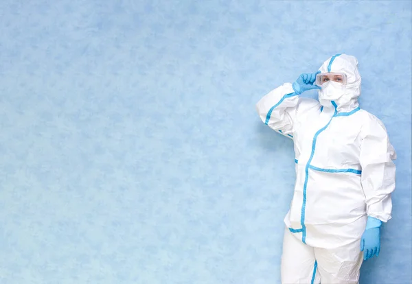 Medical worker in a white protective suit on a blue background. Wear a respirator and gloves. Place for an inscription. Panorama.