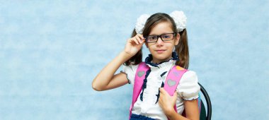 Sırtında mavi bir sırt çantasıyla okul kıyafetleri içinde gözlüklü komik siyah saçlı kız. Okul için hazırlık. Metnin için yer.