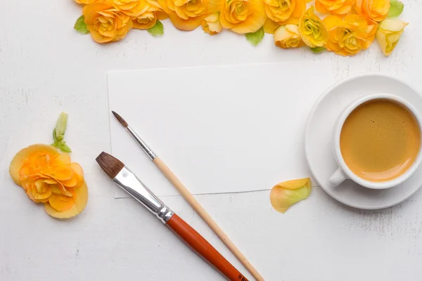 Blank notepad, flowers, brushes and cup of coffee over white woo