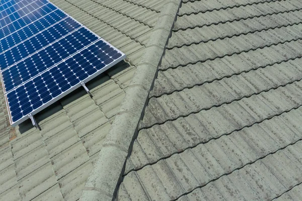 Blue solar panels on a green tiled roof in the bright sunshine