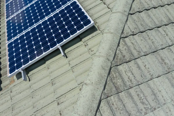 Blue solar panels on a green tiled roof in the bright sunshine