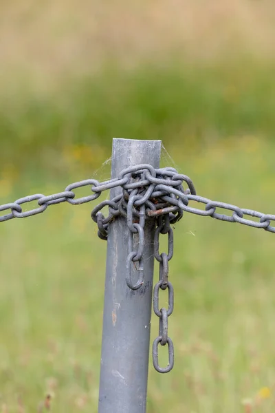 Industrial chain attached to a galvanised fence post in a green field