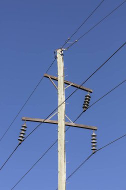 Ahşap bir telefon direğinin ve mavi gökyüzüne bağlı kabloların fotoğrafı.