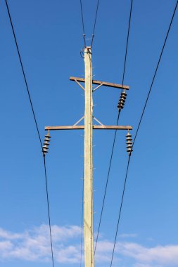 Ahşap bir telefon direğinin ve mavi gökyüzüne bağlı kabloların fotoğrafı.