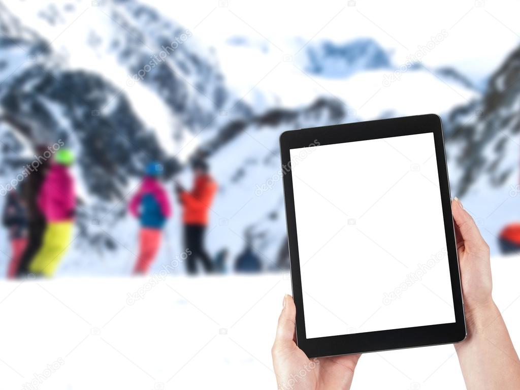 tablet in hands and people skiing in the background