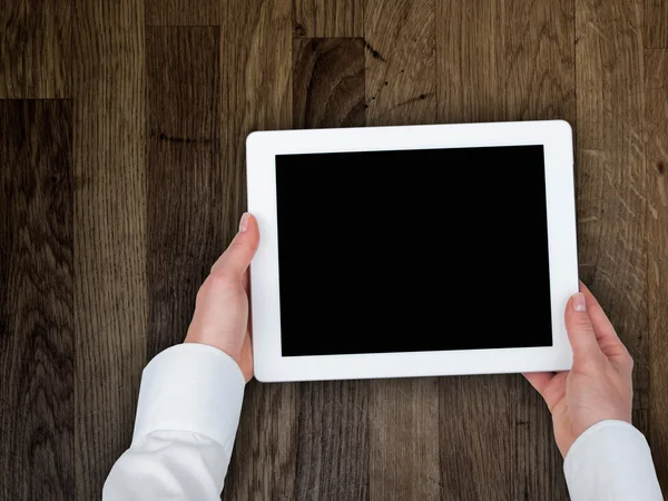 Die Hand einer Frau hält eine Tablette auf dem Hintergrund einer hölzernen Tischplatte — Stockfoto