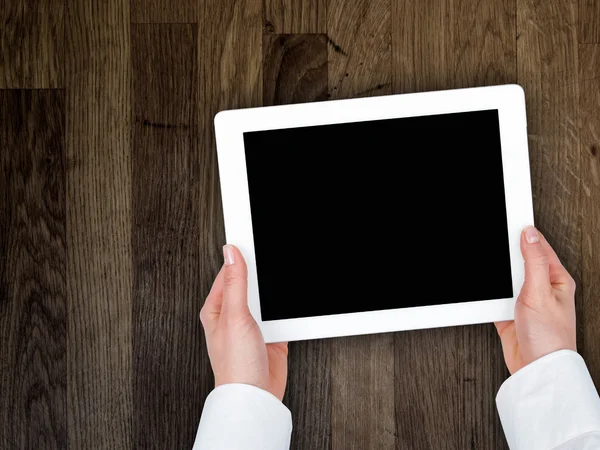 Mão da mulher segurando um tablet no fundo de uma mesa de madeira — Fotografia de Stock