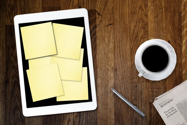 Digital tablet computer with sticky note paper and cup of coffee on old wooden desk. Simple workspace or coffee break with use of web .