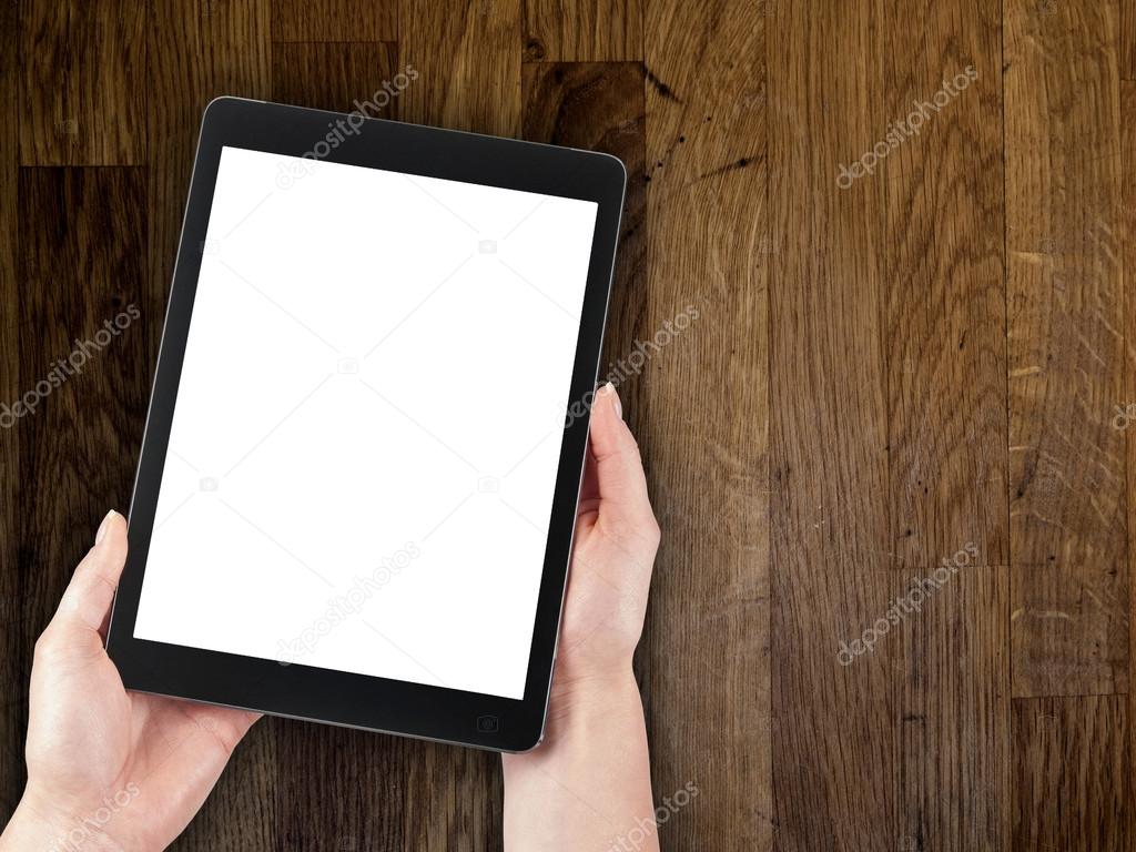 woman's hand holding a tablet on the background of a wooden tabletop