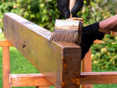 Elinde boya fırçası olan bir erkek ressamın eli. Kafkasyalı bir adam ahşap bir teras boyuyor. Boyama işi.