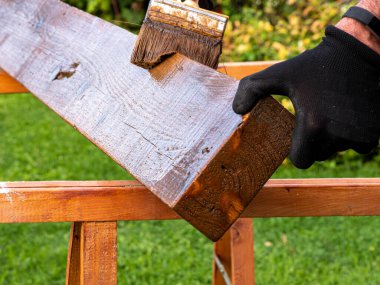 Elinde boya fırçası olan bir erkek ressamın eli. Kafkasyalı bir adam ahşap bir teras boyuyor. Boyama işi.
