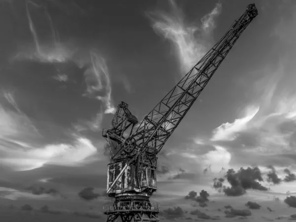 Old gantry crane in black and white photo standing at the quay of the canal in the port used for unloading. Blue sky at sunset. Beautiful photo for a photo on the wall.