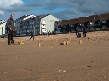 Courseulles sur Mer, Fransa, Mayıs 2021. Sahilde İskandinav Mlkky-kubb oyunu oynuyorum. Tahta bloklar sahilde duruyor ve iki adam oynuyor. Güzel güneşli zemin, Normandiya sahilleri.