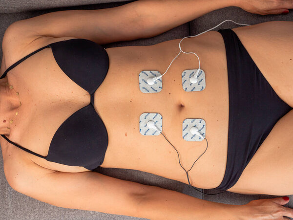 Woman in therapy with electrodes placed on abdominal muscles, post-traumatic rehabilitation, treatment