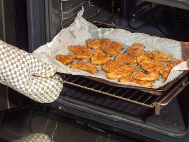 Altın kaplama pirzolalar fırından bir mutfak eldiveni kullanılarak çıkarılıyor. Çıtır çıtır pişmiş kaplama görünür..