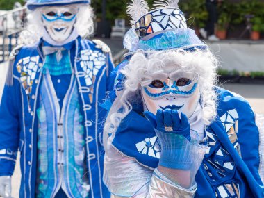 Büyülü Karnaval Öpücüğü, aynalar, tüyler ve maviliklerle dolu büyüleyici kostümler içinde, karnaval katılımcıları peri masalı gizemi havası yayıyorlar.