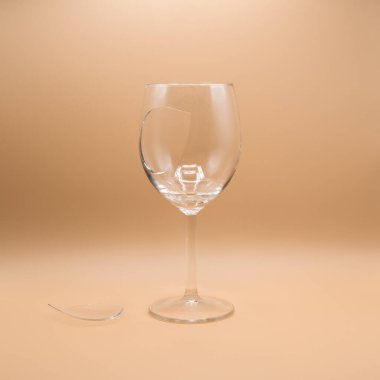 Bej bir arka planda kırık bir şarap kadehi yanında da kayıp bir parça var. Kırılganlığın ve hasarın sembolü..