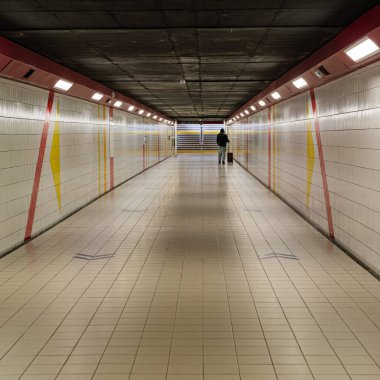 Bavullu bekar bir adam yeraltı yaya tünelinde yürüyor. Seyahat, yolculuk, kentsel yalnızlık, geçiş ve modern şehir ulaşım altyapısı kavramı.